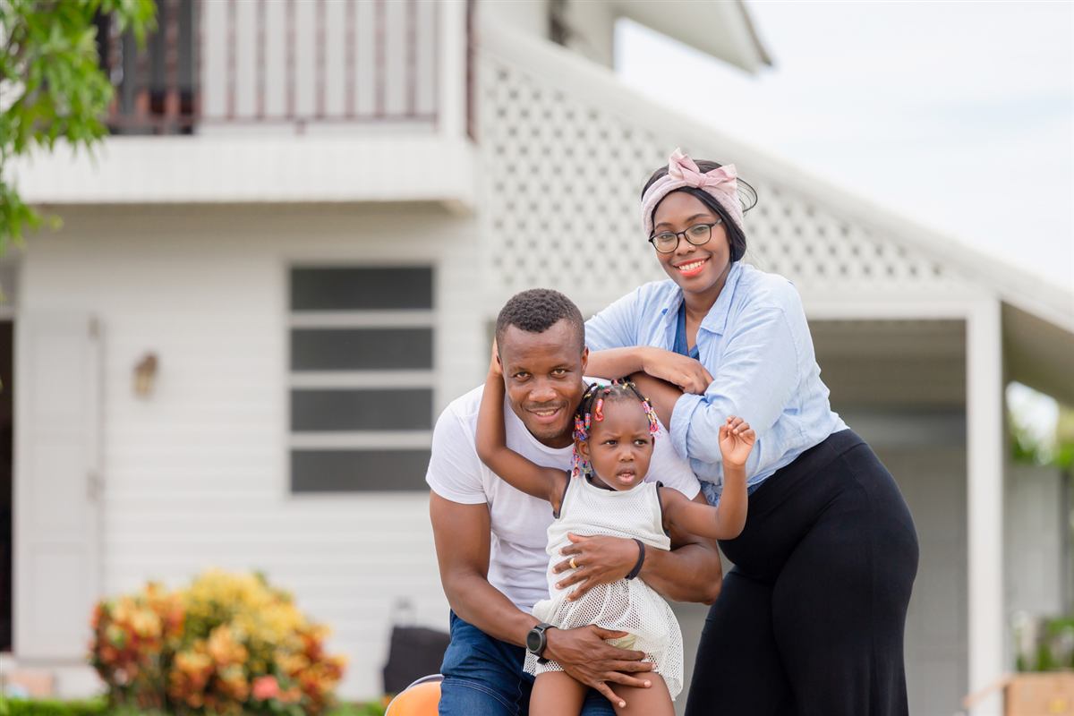 A smiling family with a young child outside their new home