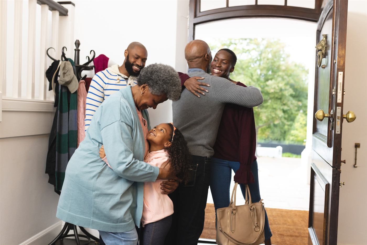 A family greeting each other with hugs at the front door of a home