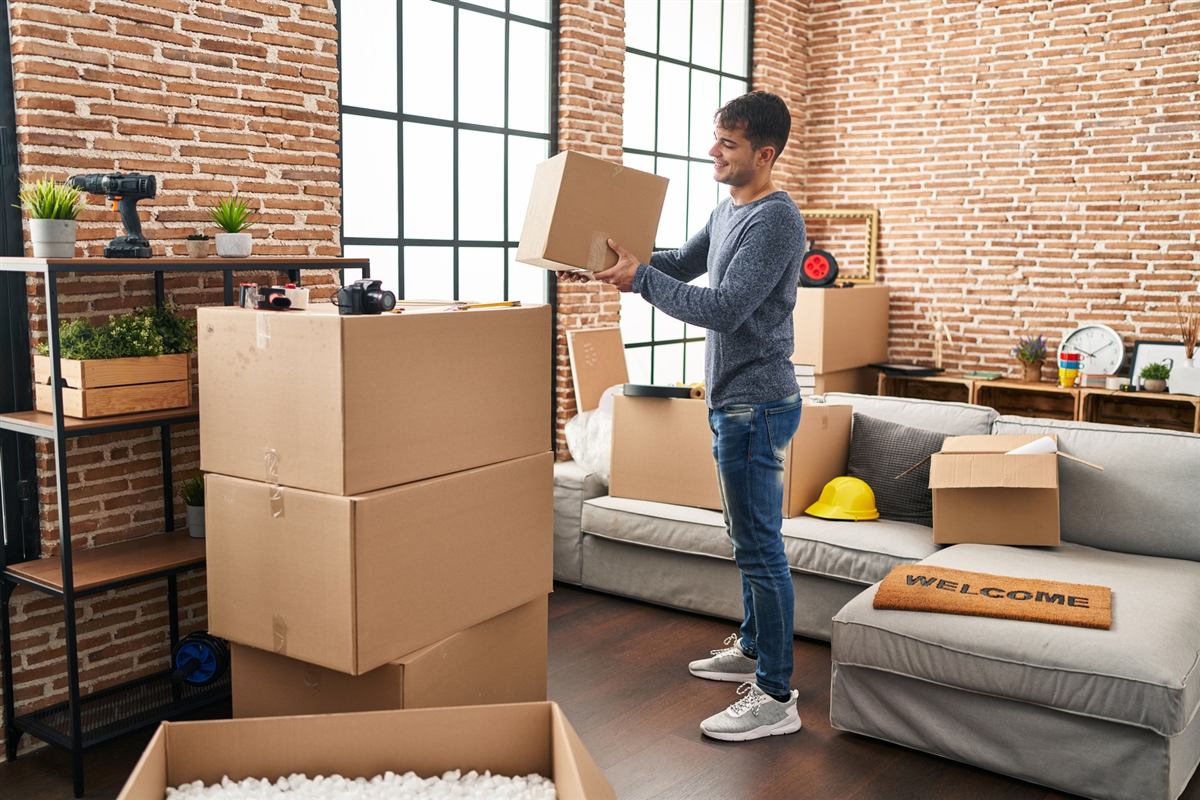 A young man smiling as he carries a box into his first apartment